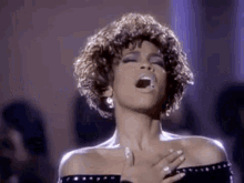 a woman is singing into a microphone while holding her hands to her chest .