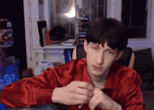 a man in a red shirt is sitting in front of a window