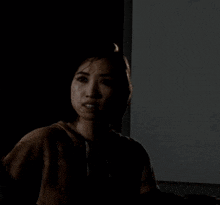 a woman in a brown hoodie is looking at the camera