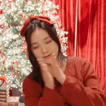 a woman wearing a red sweater and a red bow in her hair applauds in front of a christmas tree