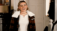 a woman wearing a plaid jacket and a white shirt is standing next to a staircase and smiling .