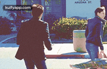 two men are walking down a sidewalk in front of a building that says arizona st. on it