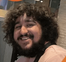 a man with a beard and curly hair is smiling for the camera .