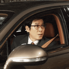 a man wearing glasses and a suit is sitting in a car