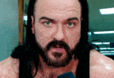 a man with long black hair and a beard is talking into a microphone .