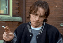 a man wearing glasses is smoking a cigarette in front of a brick building