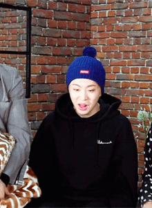 a person wearing a blue supreme beanie and a black hoodie