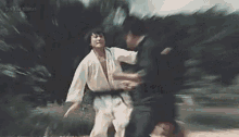 a man in a white karate uniform is fighting another man in a black belt in a park .