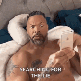 a shirtless man is laying on a bed looking at his phone .