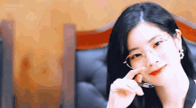 a woman wearing glasses is holding a pen to her nose and smiling .