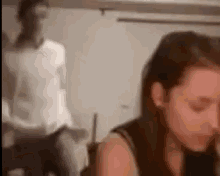 a blurry picture of a woman sitting at a table with a man standing in the background .