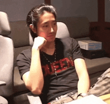 a man wearing a black shirt with the word rush on it sits in a chair