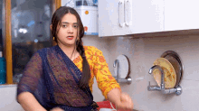 a woman in a blue and yellow dress is washing dishes in a kitchen sink .