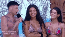 a man is talking into a microphone while two women in bikinis smile .