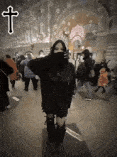 a woman covering her face in front of a crowd with a cross above her head