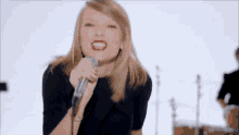 taylor swift is singing into a microphone in front of a drum set .