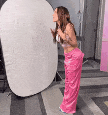 a woman in pink pants and a crop top stands in front of a white backdrop
