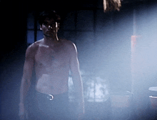 a shirtless man stands in a dark room with a belt around his waist