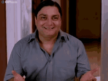 a man in a blue shirt is smiling and making a funny face while standing in front of a door .