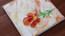 a painting of a flower with a green stem is on a wooden table