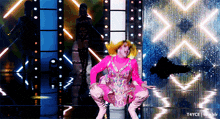 a woman in a pink dress is squatting down on a stage with a tumblr logo in the corner
