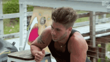 a man in a black tank top is sitting on a wooden stool .
