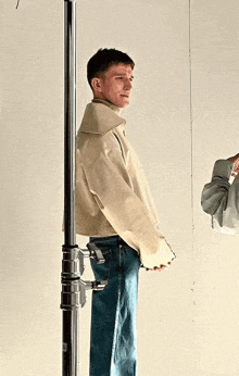 a man wearing a white jacket and blue jeans is standing next to a metal pole