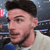 a man with a beard is talking into a microphone while wearing a sweater .