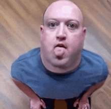 a bald man in a blue shirt is sticking out his tongue .