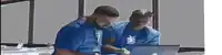 two men in blue shirts look at a laptop