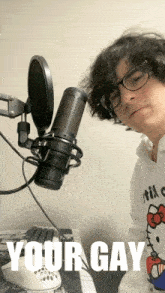 a man wearing glasses and a hello kitty shirt stands in front of a microphone with the words " your gay " written below him