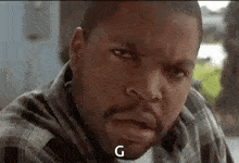 ice cube is making a funny face while wearing a plaid shirt and smoking a cigarette .