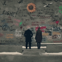 two men are standing in front of a wall that has graffiti on it including the words fight and revolt