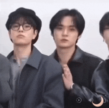 a group of young men are standing next to each other . one of the men is wearing glasses and a hat .