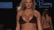 a woman in a bikini walks down a runway in front of a sign that says bunny swimsuit