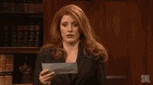 a woman is holding a piece of paper in front of her face and her hair is blowing in the wind .