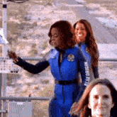 a group of women in blue jumpsuits are standing next to each other on a bridge .