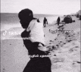 a black and white photo of a man walking on a beach with arabic writing .