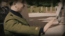 a man in a green suit is driving a car while another man looks on .