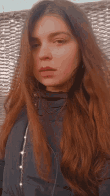 a woman with long brown hair wearing a black jacket looks at the camera