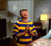 a man wearing a blue and yellow striped shirt is praying in a bedroom