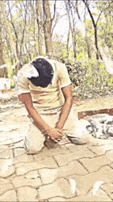 a man is kneeling down on a brick sidewalk with his head in a bucket of water .