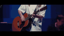 a woman in a white shirt is playing a brown guitar