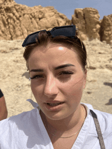 a woman wearing sunglasses looks at the camera with a rock in the background