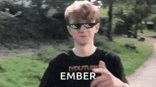 a young man wearing sunglasses and a black shirt is giving a thumbs up in a park .