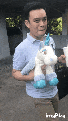 a man holding a stuffed unicorn with a blue mane