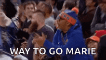 a man in a blue hoodie is sitting in a crowd of people and shouting .