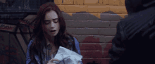 a woman is holding a piece of paper in front of a brick wall