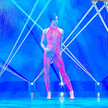 a woman in a pink jumpsuit is dancing on a stage in front of a blue background