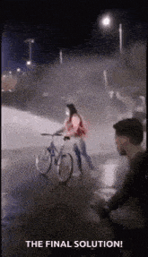 a woman is riding a bike down a street at night while a man watches .